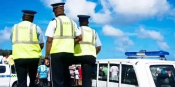 Three RSLPF officers in high-visibility vests beside a marked police vehicle during the Anse La Raye arrest operation.