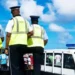 Three RSLPF officers in high-visibility vests beside a marked police vehicle during the Anse La Raye arrest operation.