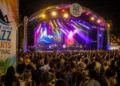 Large crowd at the Saint Lucia Jazz Festival main stage at night with colorful stage lighting and official festival branding visible.
