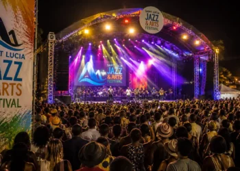 Large crowd at the Saint Lucia Jazz Festival main stage at night with colorful stage lighting and official festival branding visible.