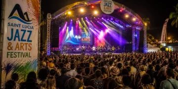Large crowd at the Saint Lucia Jazz Festival main stage at night with colorful stage lighting and official festival branding visible.