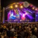 Large crowd at the Saint Lucia Jazz Festival main stage at night with colorful stage lighting and official festival branding visible.