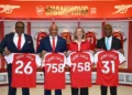 Arsenal deal officials hold Saint Lucia jerseys inside Emirates Stadium dressing room at partnership signing