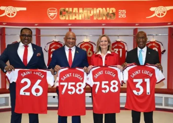 Arsenal deal officials hold Saint Lucia jerseys inside Emirates Stadium dressing room at partnership signing