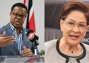 Dr. Amery Browne speaking at a podium beside Prime Minister Kamla Persad-Bissessar in Caricom Barnett row image.
