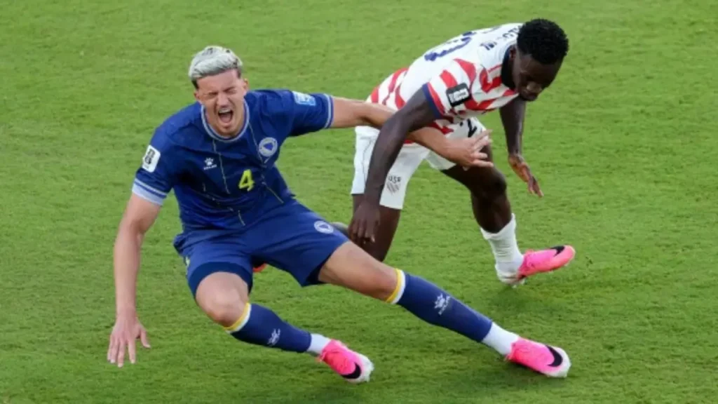 Folarin Balogun and a Bosnia and Herzegovina defender fall to the ground during a challenge at the 2026 World Cup.
