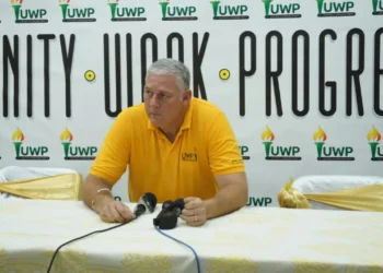Allen Chastanet seated before a UWP Unity, Work, Progress backdrop as commentary examines UWP internal divisions and party leadership.