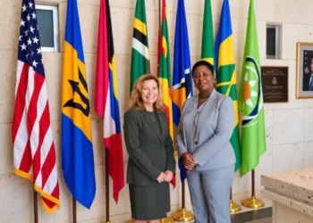 Grenada Opposition Leader Emmalin Pierre stands with a US diplomat beside Caribbean and US flags.