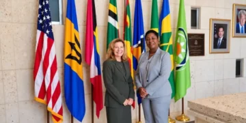 Grenada Opposition Leader Emmalin Pierre stands with a US diplomat beside Caribbean and US flags.
