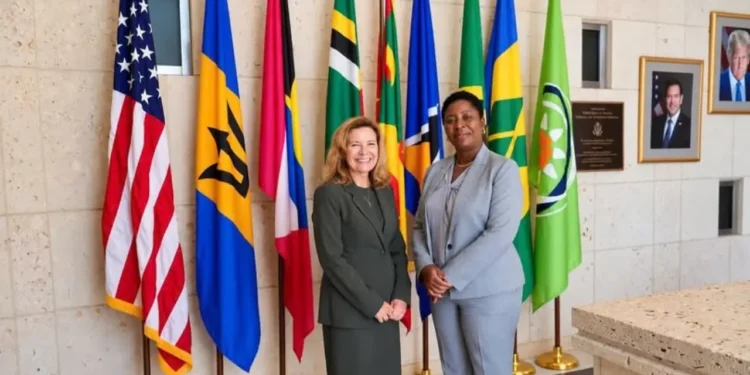 Grenada Opposition Leader Emmalin Pierre stands with a US diplomat beside Caribbean and US flags.