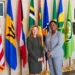 Grenada Opposition Leader Emmalin Pierre stands with a US diplomat beside Caribbean and US flags.