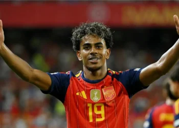 Lamine Yamal celebrates with both arms raised while wearing Spain’s red jersey.