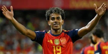 Lamine Yamal celebrates with both arms raised while wearing Spain’s red jersey.